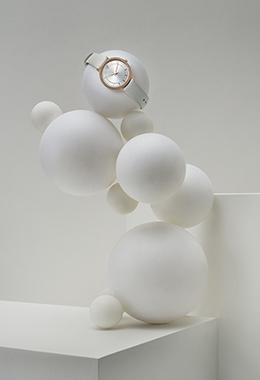 Women's watch with crystals placed on a composition of Christmas baubles on a white geometric background.
