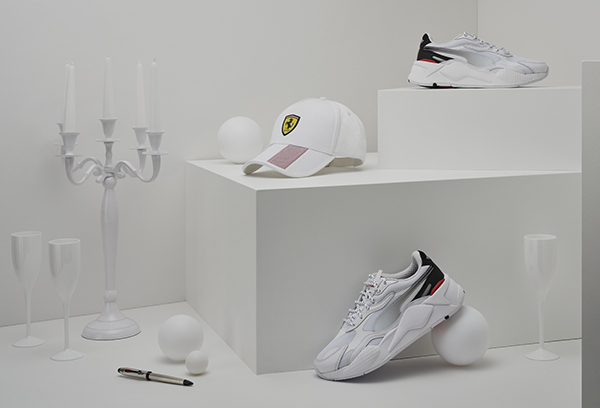Scuderia Ferrari shoes and accessories on a white geometric background with a candlestick, some glasses and Christmas baubles.
