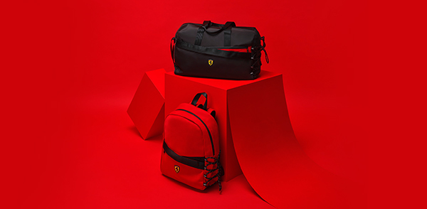 Black institutional travel bag with Shield and red institutional rucksack with Shield on red geometric blocks.