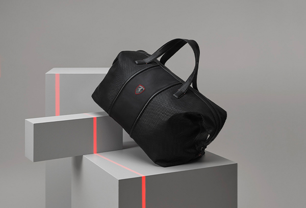 Black Hypergrid shoulder bag in perforated technical fabric and leather on grey geometric blocks with red light effects.