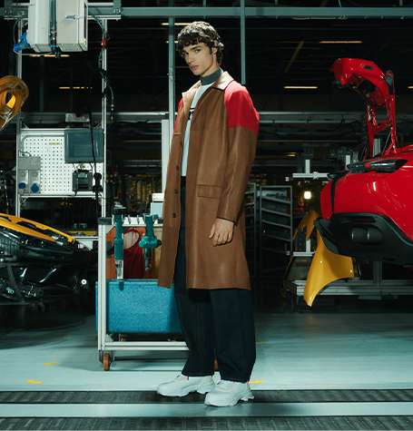Full-length picture of a man wearing brown and red car coat leather jacket inside Ferrari factory