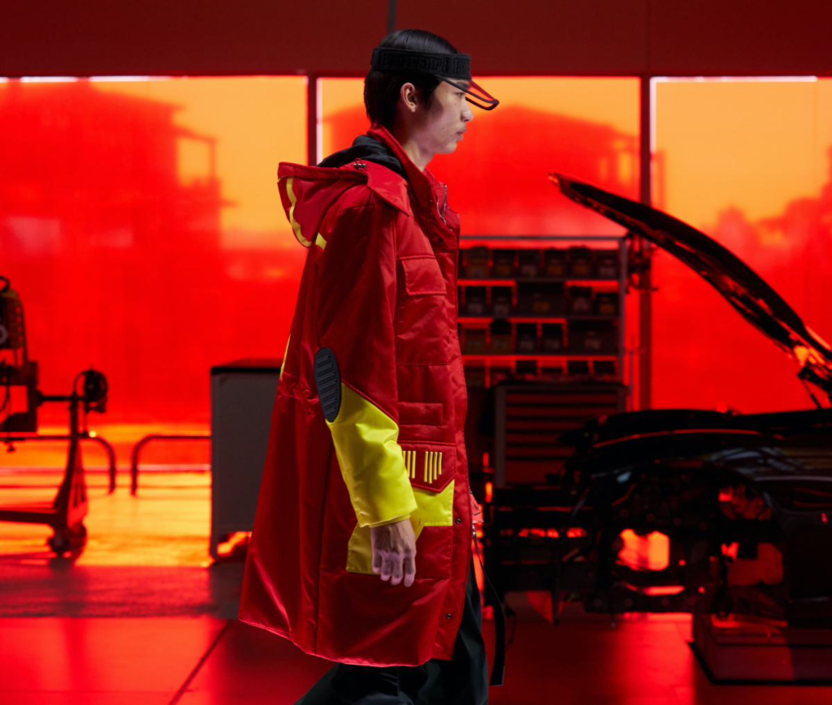 Model on the catwalk wearing black visor and red parka