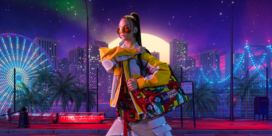 Woman on a metropolitan background with neon lights wearing the two-tone cotton blouson, printed canvas shopper bag and Ferrari sunglasses